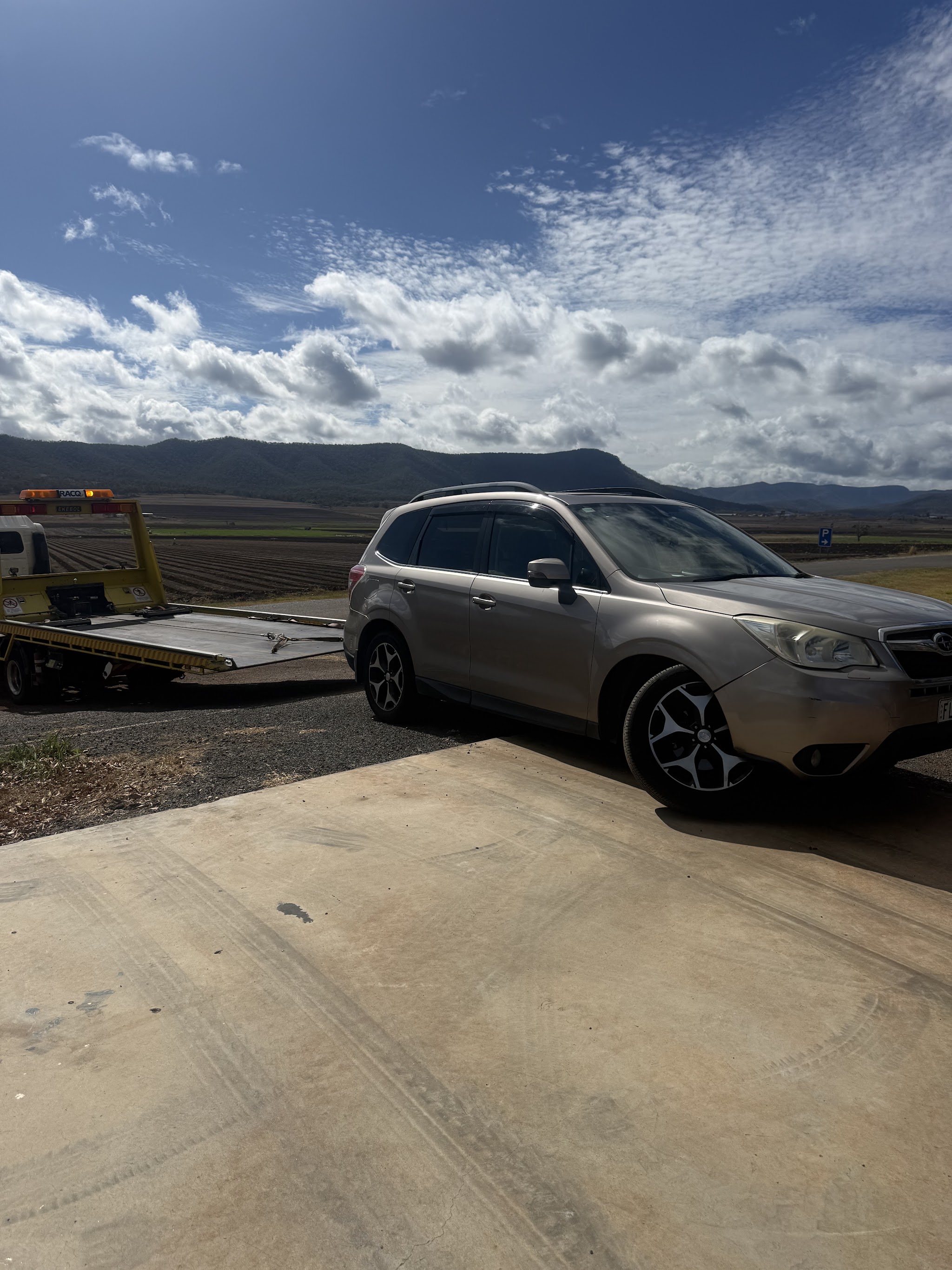 A Subaru Forester on the Southern Downs Mechanical driveway beside a tow truck, with the range in the background