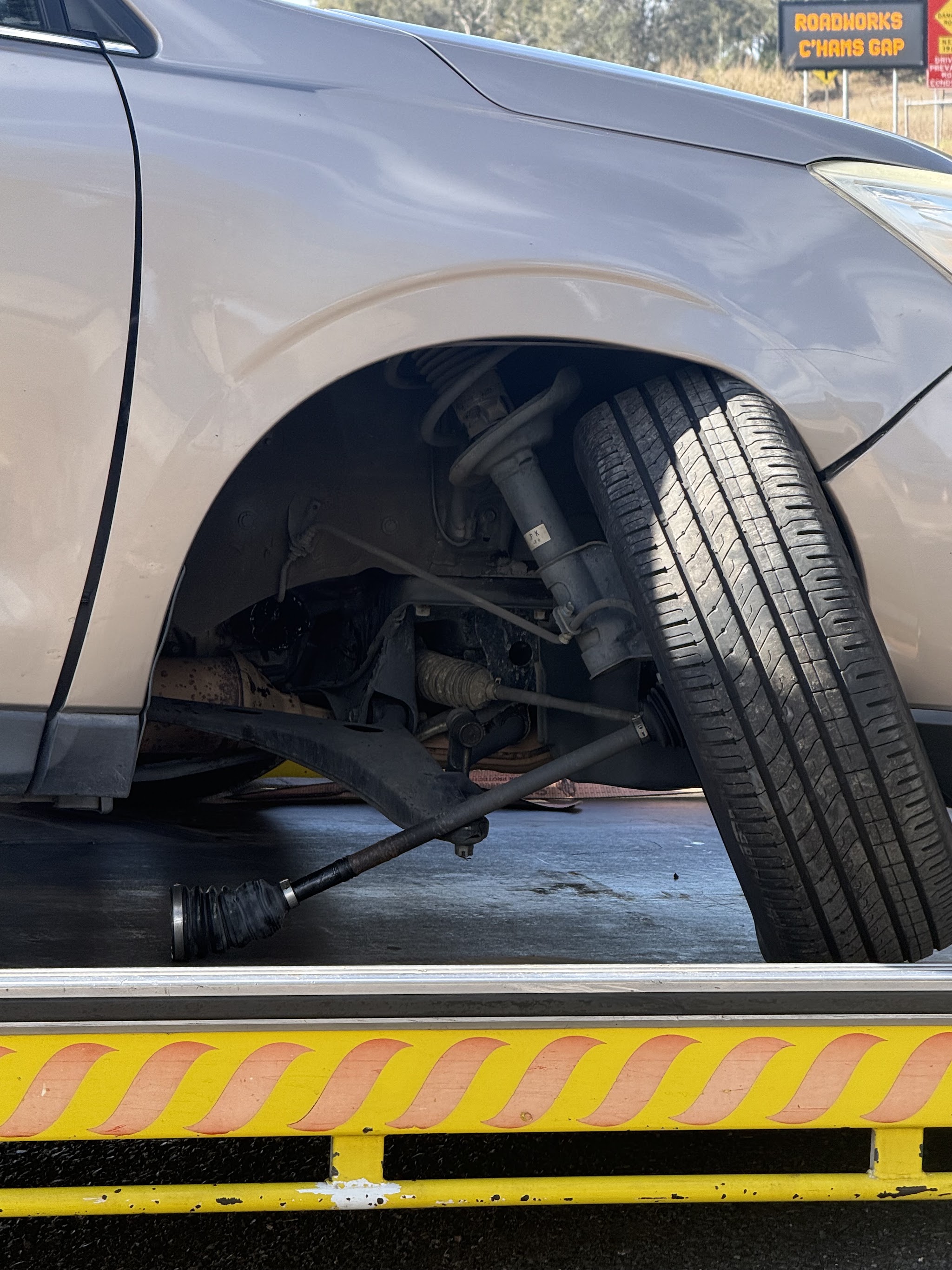 A snapped front suspension arm hanging beneath a car on a tow truck deck near Cunningham's Gap